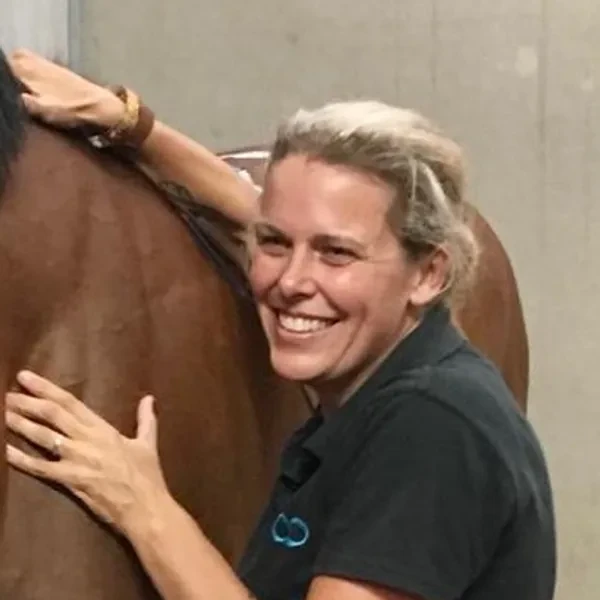 Robyn Taylor working on a bay horse in a stable